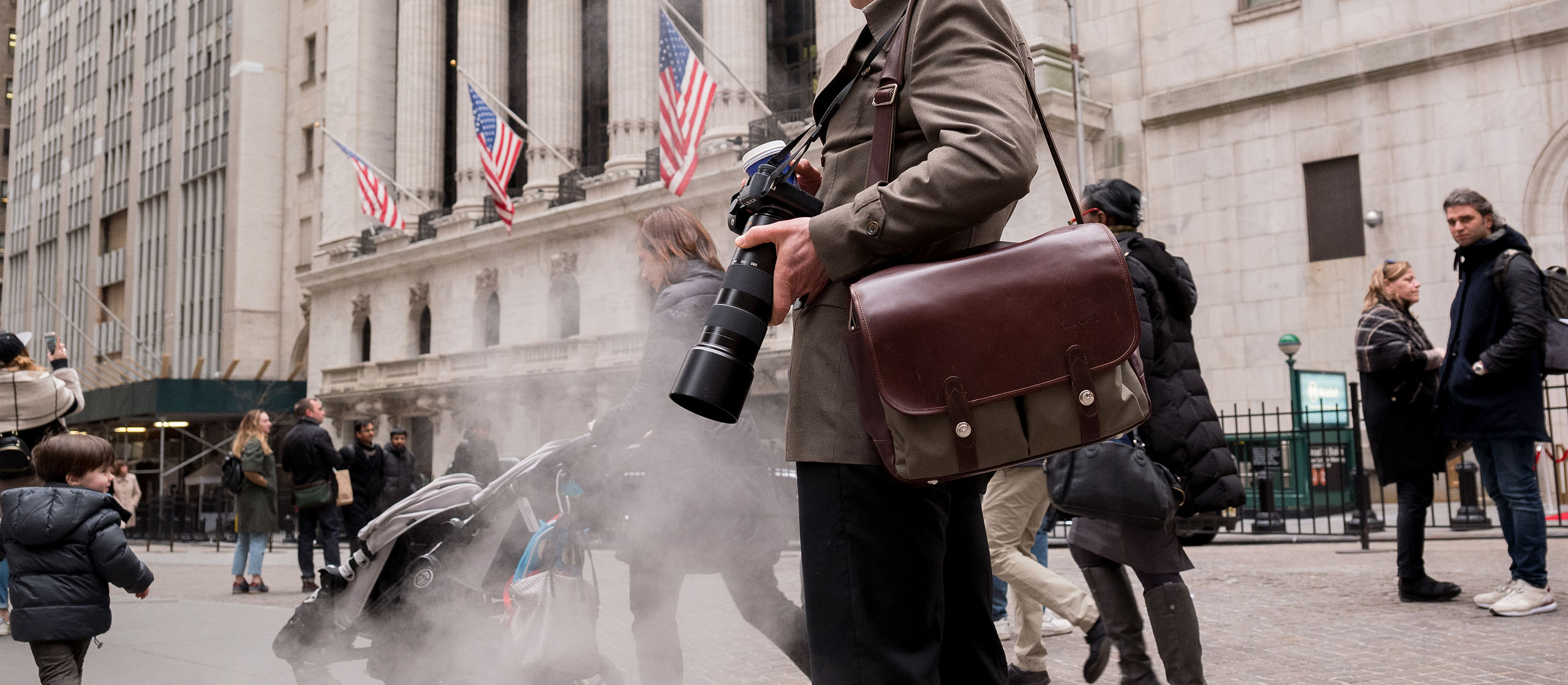 Mann mit einer Kamera in der Hand steht mit einer Oberwerth Kameratasche aus Leder um die Schulter auf dem Platz vor einem amerikanischen Gebäude