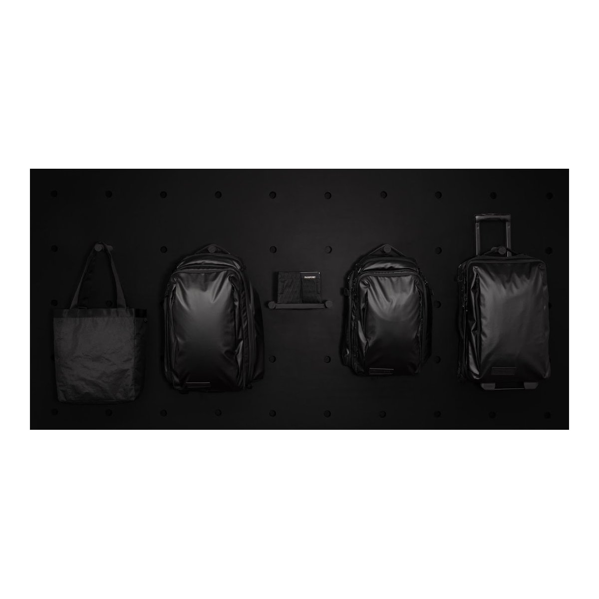 WANDRD Travel Wallet - Produktsortiment: Schwarze Tote Bag, zwei Rucksäcke, ein Trolley und ein Dokumentenhalter auf schwarzer Wand.
