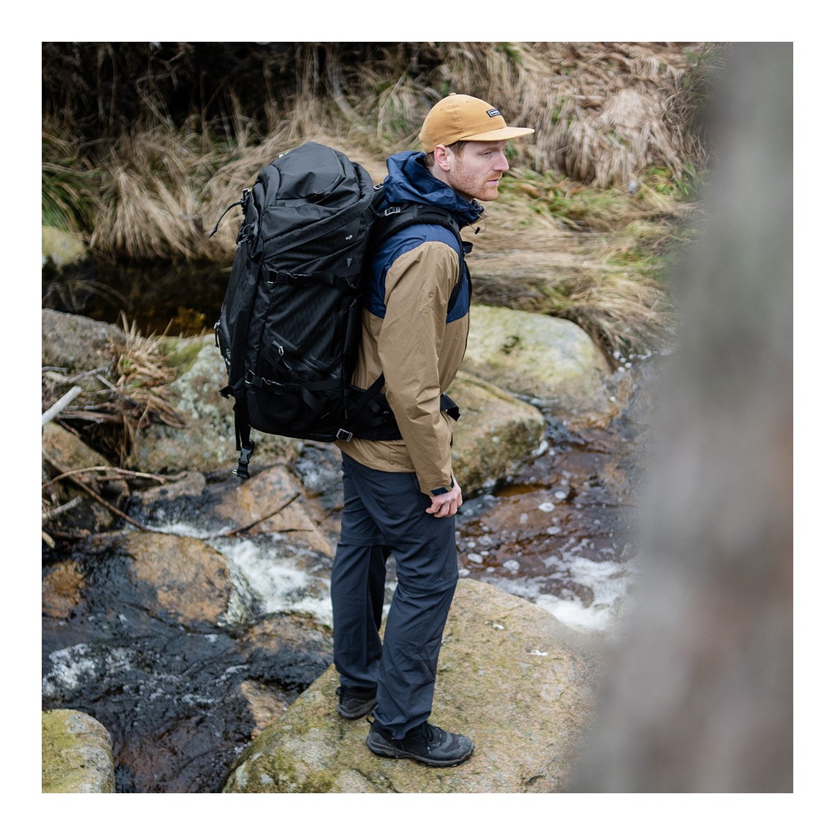 F-Stop DuraDiamond Shinn Essentials Bundle - Anthrazit - Anwendungsbeispiel: Mann von der Seite trägt schwarzen Wanderrucksack am Flussufer.