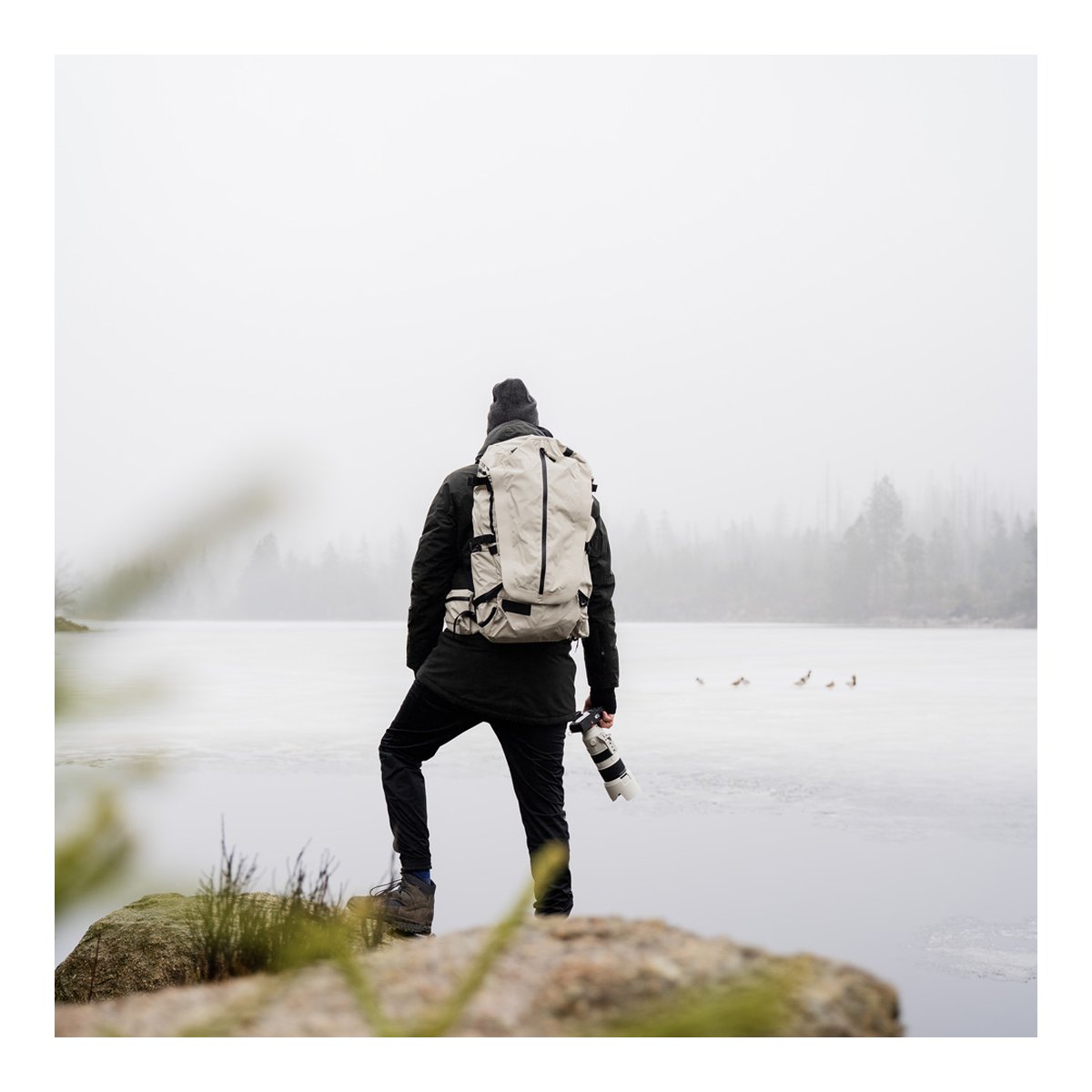 Wandrd Fernweh M/L Tan Photo Bundle - Anwendungsbeispiel: Rückansicht Person mit Rucksack und Kamera am zugefrorenen See.