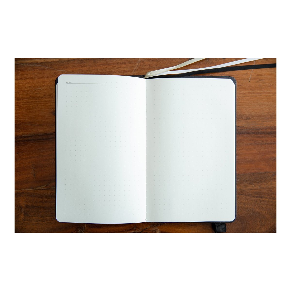 WANDRD NOTEBOOK Yellow - Innenansicht: Geöffnetes Notizbuch auf Holztisch mit blanko gepunkteten Seiten, Datumsfeld und Lesezeichen.