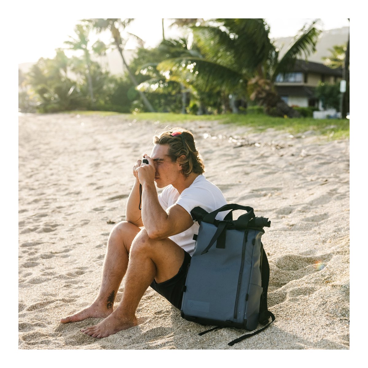WANDRD PRVKE Lite 11-Liter Blue - Anwendungsbeispiel: Mann mit grauem Rucksack sitzt am Strand und fotografiert. WANDRD PRVKE Lite 11-Liter Blue - Anwendungsbeispiel: Mann mit grauem Rucksack sitzt am Strand und fotografiert.
