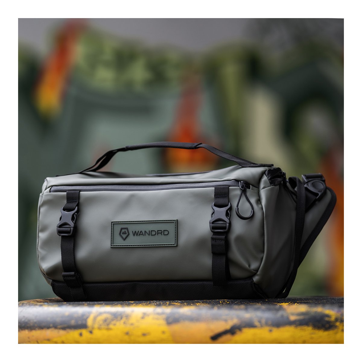 WANDRD ROGUE Sling 9L Wasatch Green - Vorderansicht der grauen WANDRD Sling Bag auf gelbem Metall, mit Logo und Schnallen.