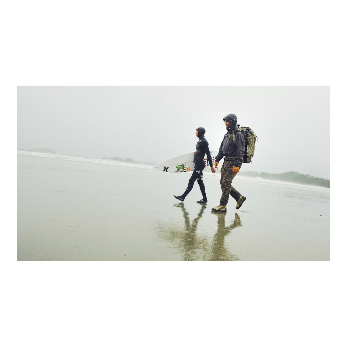 F-Stop Sukha Anthrazit (Schwarz) - Anwendungsbeispiel: Zwei Abenteurer, einer mit Surfbrett, der andere mit Rucksack, gehen am regnerischen Strand. F-Stop Sukha Anthrazit (Schwarz) - Anwendungsbeispiel: Zwei Abenteurer, einer mit Surfbrett, der andere mit Rucksack, gehen am regnerischen Strand.