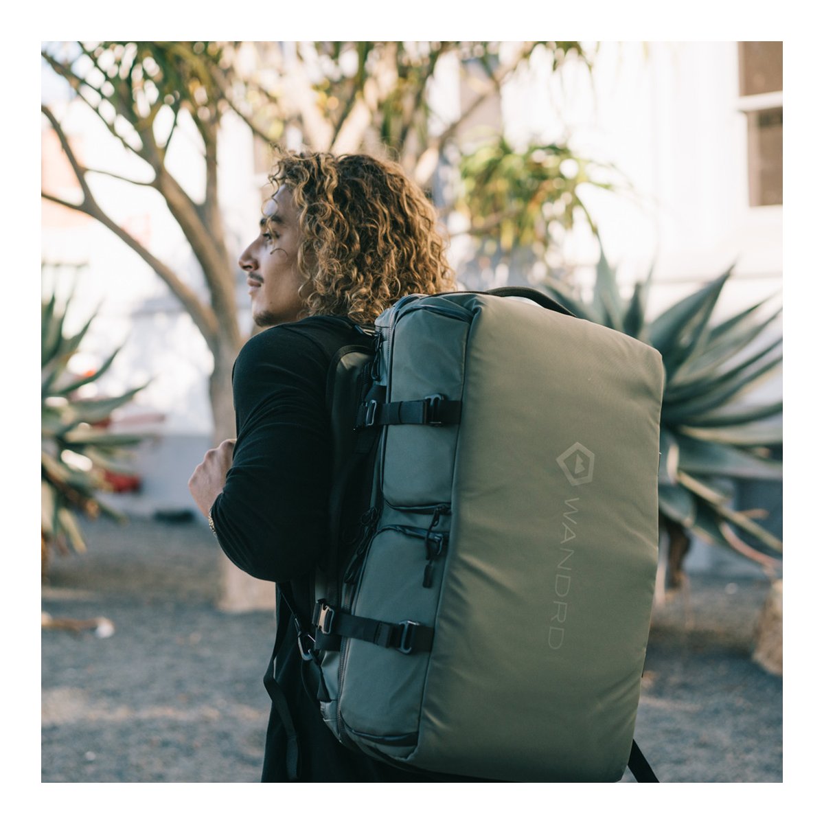 WANDRD HEXAD ACCESS DUFFEL Wasatch Green - Anwendungsbeispiel: Mann trägt Rucksack im Profil, Seitenansicht mit Logo WANDRD HEXAD ACCESS DUFFEL Wasatch Green - Anwendungsbeispiel: Mann trägt Rucksack im Profil, Seitenansicht mit Logo