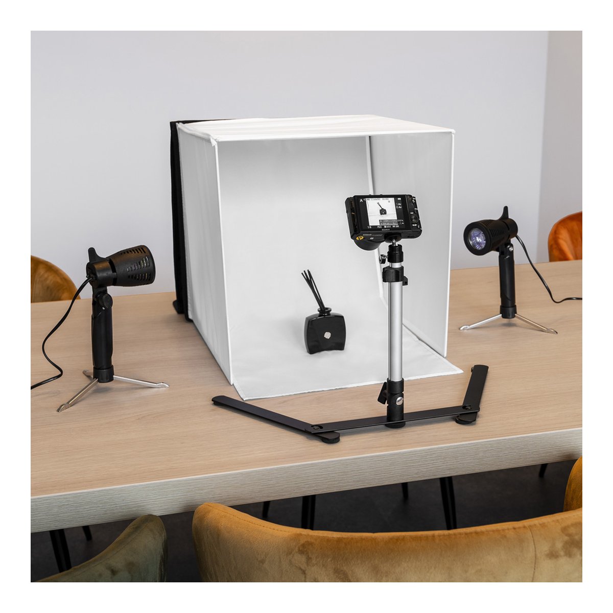 Caruba Tragbares Fotostudio 40x40x40cm mit Separaten Halogenlampen - Anwendungsbeispiel: Smartphone-Fotostudio-Setup mit Lichtbox, Handy-Stativ und zwei LED-Lampen auf Holztisch.