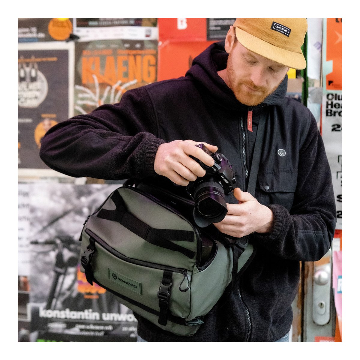 WANDRD ROGUE Sling 9L Wasatch Green - Anwendungsbeispiel: Mann nimmt Kamera aus grauer Umhängetasche.