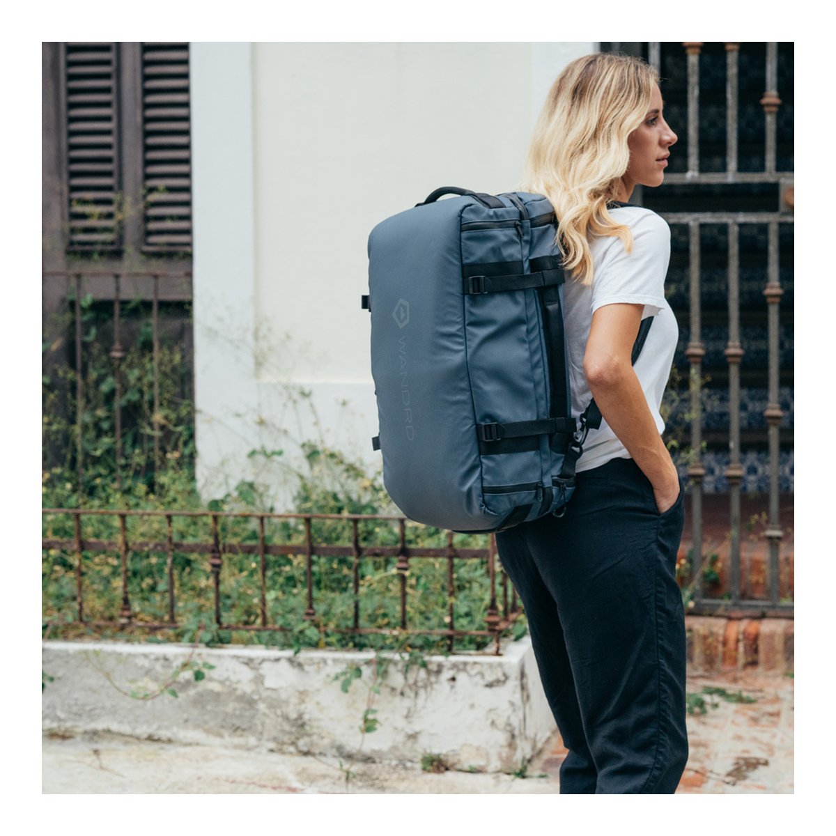 WANDRD HEXAD ACCESS DUFFEL Aegean Blue - Anwendungsbeispiel: Blaugrauer Rucksack an Frau, seitliche Ansicht.