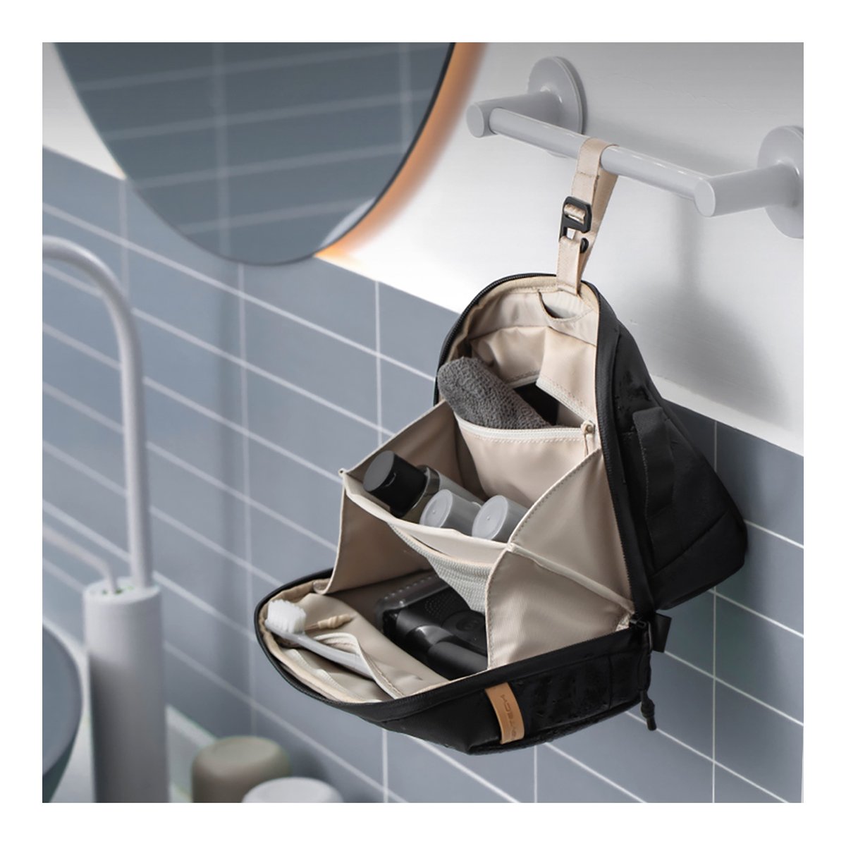 PGYTECH Wash Pouch(Twilight Black) - Produkt in Anwendung: Schwarzer Kulturbeutel mit geöffneten Fächern, an Handtuchhalter im Bad hängend, gefüllt mit Pflegeprodukten.