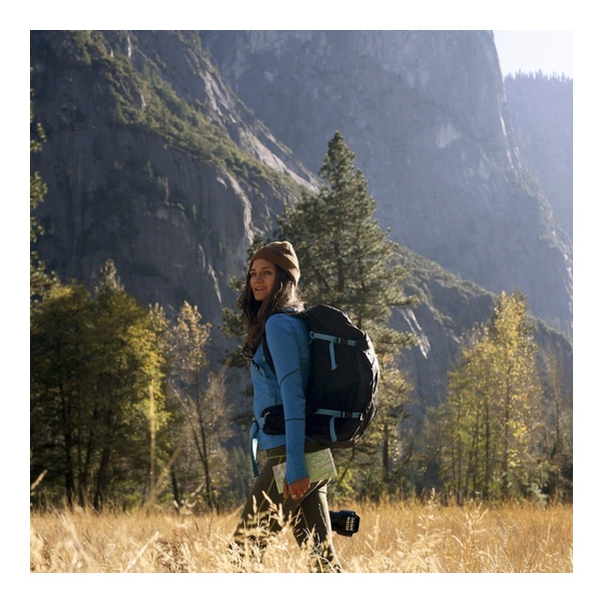 F-Stop Kashmir UL Black / Malibu Blue - Anwendungsbeispiel: Eine Wanderin trägt den Rucksack in einem Feld vor einer Bergkulisse.