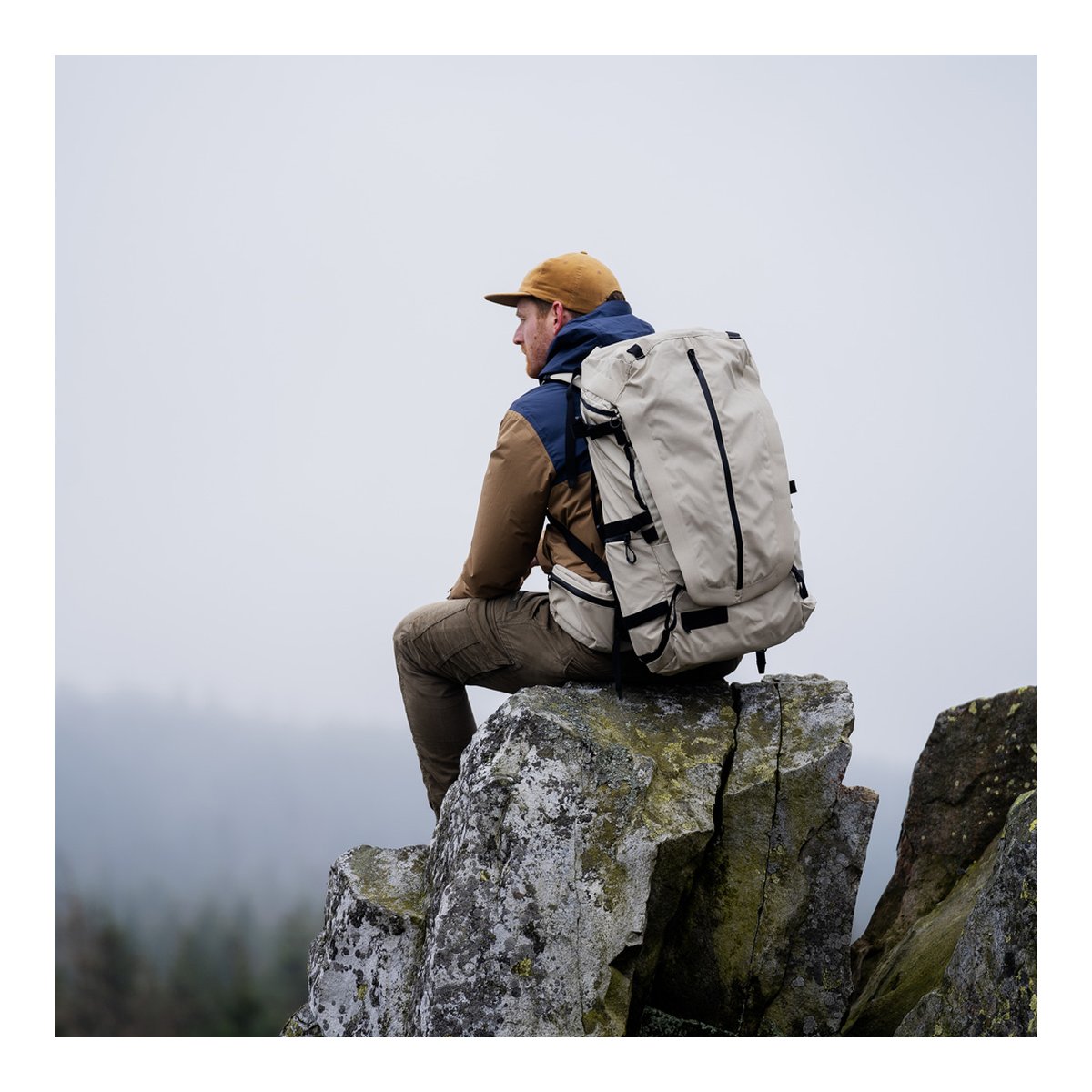 Wandrd Fernweh M/L Tan Photo Bundle - Anwendungsbeispiel: Beiger Rucksack am Rücken einer Person, sitzend auf Felsen in Natur.