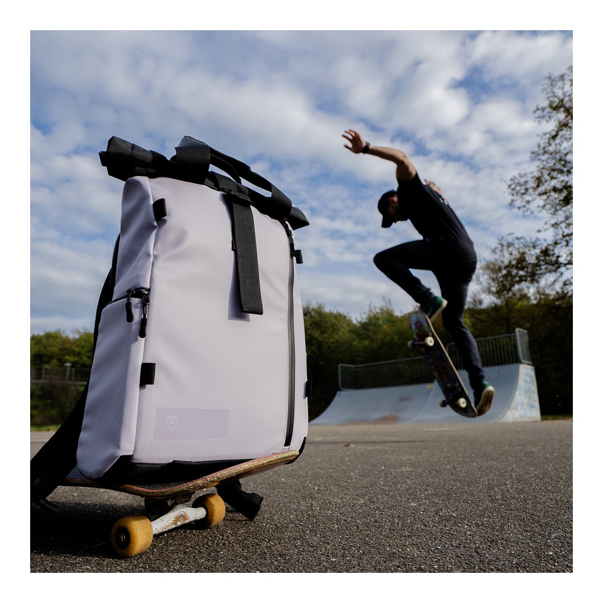 WANDRD PRVKE Lite 11-Liter Uyuni Purple - Anwendungsbeispiel: Heller Roll-Top Rucksack auf Skateboard im Skatepark, Skater im Hintergrund