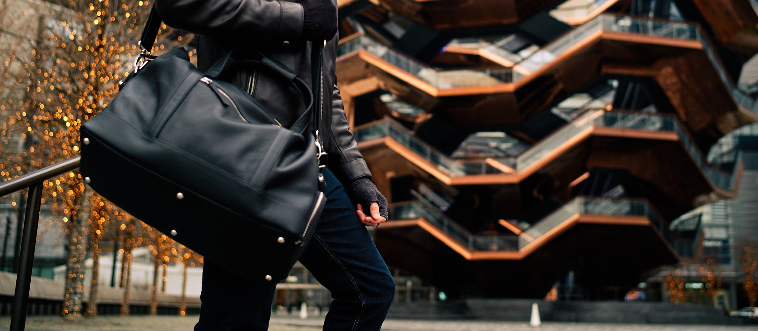 Mann steht mit einer Oberwerth Reisetasche aus Leder die ihm über die Schulter hängt vor einem Gebäude