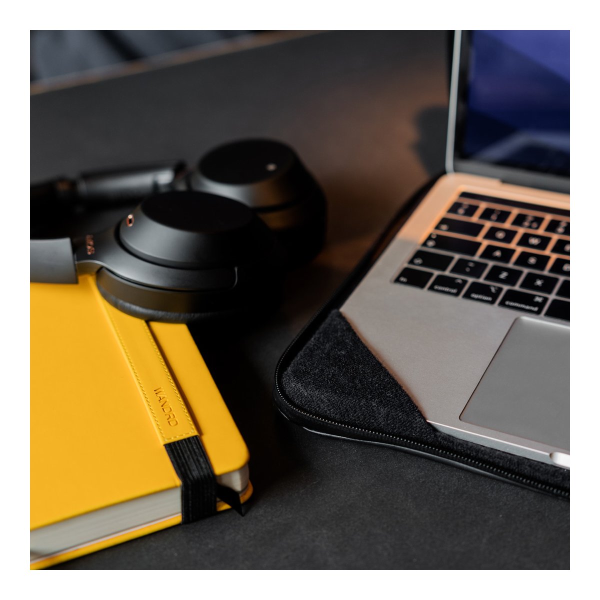 WANDRD Laptop-Tasche 14" Schwarz - Anwendungsbeispiel: Laptop in Schutzhülle auf Schreibtisch mit Notizbuch und Kopfhörern