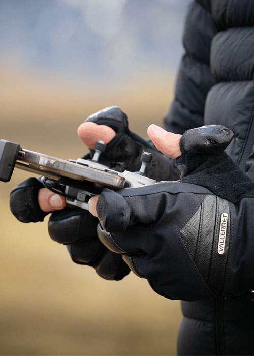 Person mit Winter-Fotohandschuhen steuert ein Gerät, Fingerkuppen sind freigelegt für präzise Bedienung.