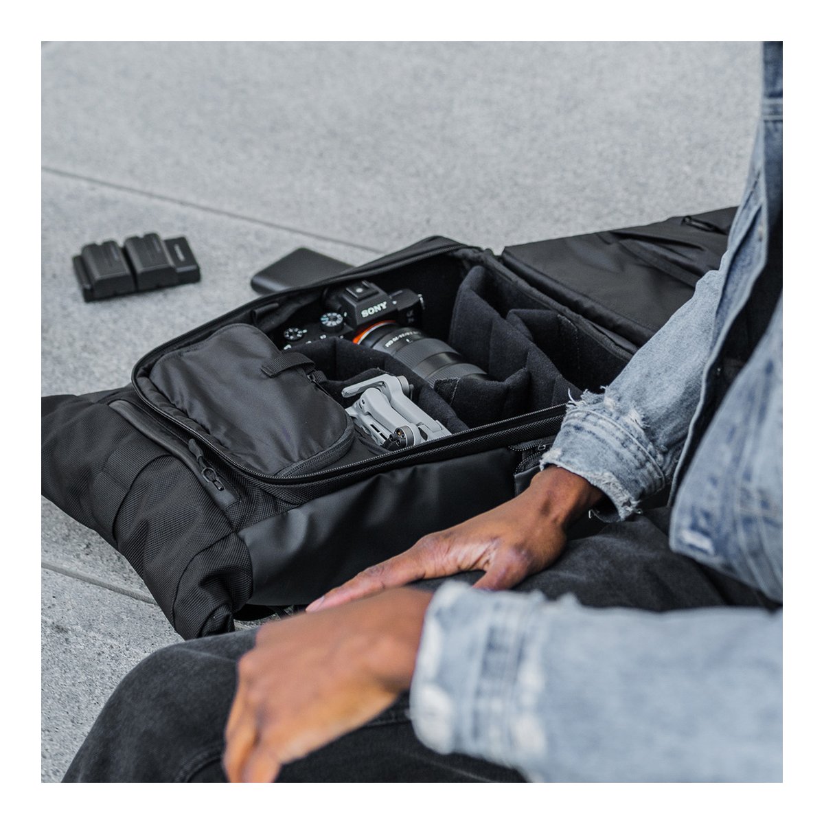 WANDRD PRVKE Lite 11-Liter Black - Anwendungsbeispiel: Geöffnete schwarze Tasche mit Kamera, Drohne und Zubehör auf dem Boden.