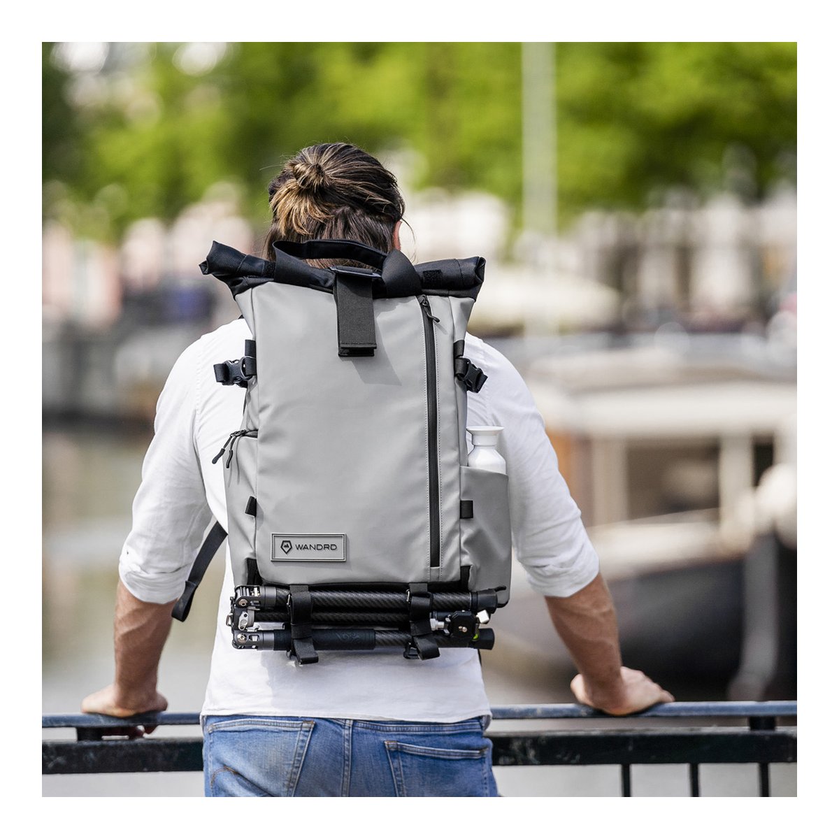 WANDRD PRVKE 31-Liter DisNet Grey Photo Bundle - Rückansicht: Grauer Rucksack im Anwendungsbeispiel, an Person getragen mit Stativ und Wasserflasche.