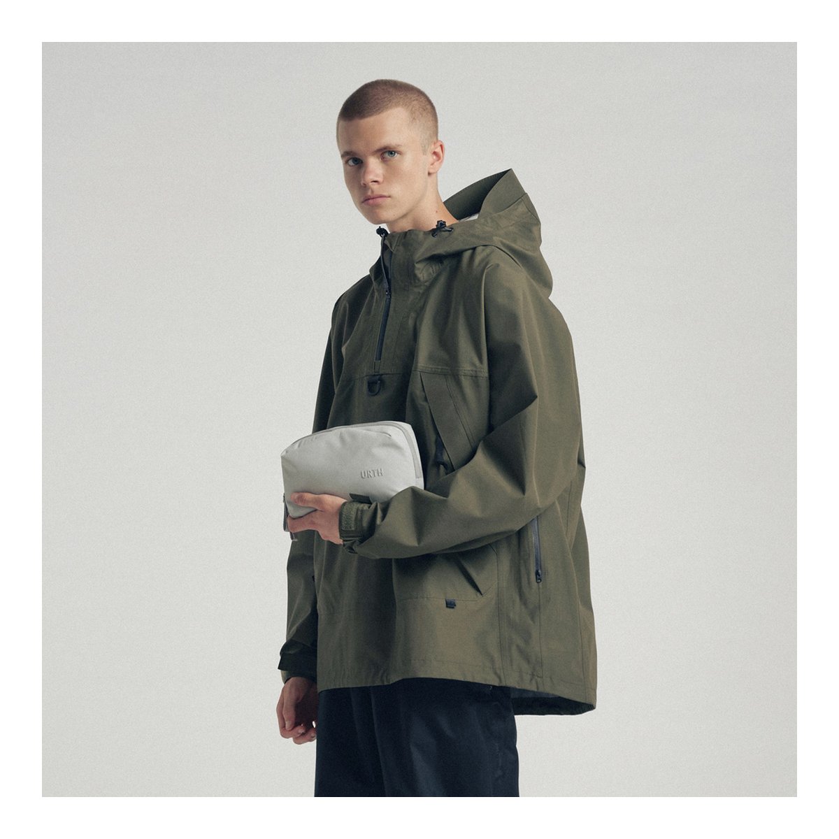 Urth Zeolite Tech Organiser(Aschgrau) - Model in olivgrüner Jacke hält URTH Tasche.