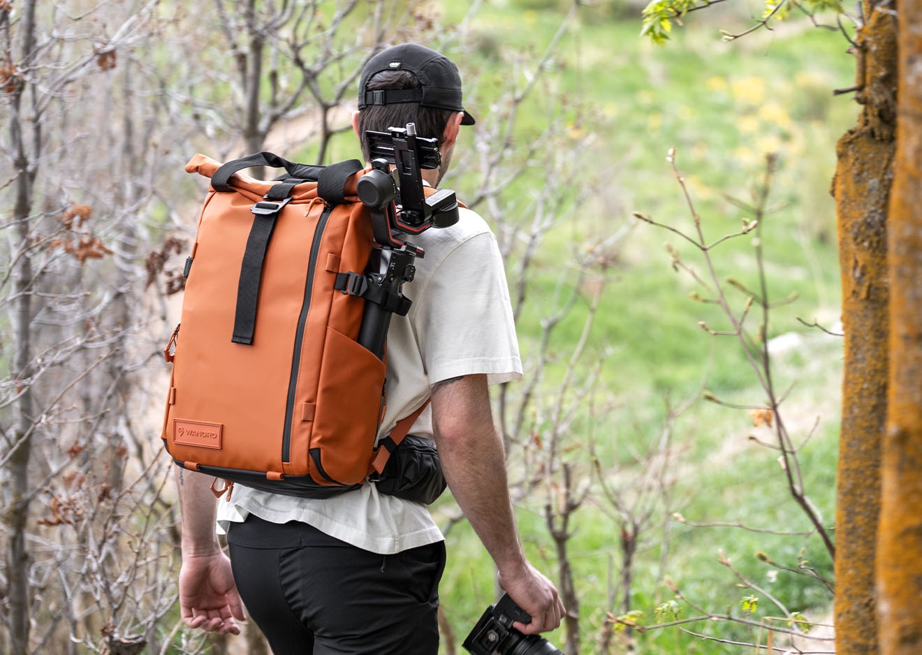 Mann mit orangem Wandrd PRVKE Rucksack und Stativ unterwegs in der Natur
