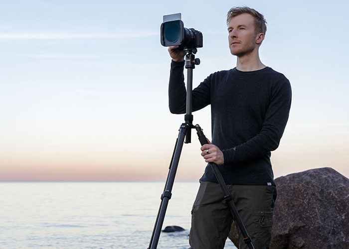Rollei C5i und C6i Carbonstativ: Fotograf richtet Kamera am Stativ am Meer aus
