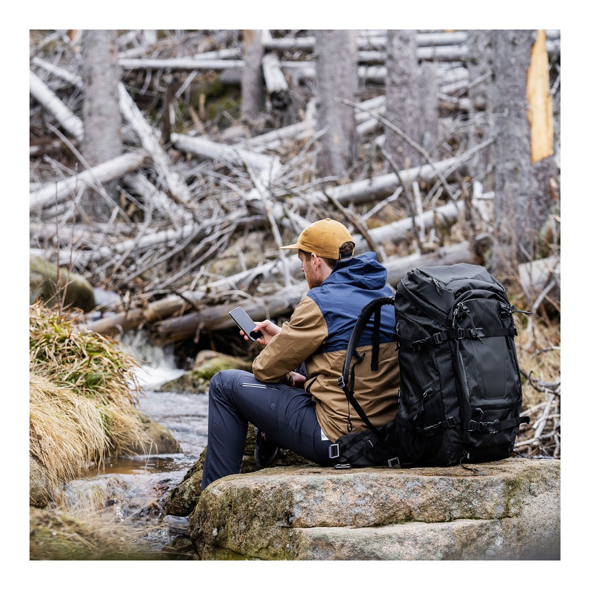 F-Stop DuraDiamond Shinn Essentials Bundle - Anthrazit - Anwendungsbeispiel: Mann mit schwarzem Rucksack im Wald am Bach nutzt Smartphone