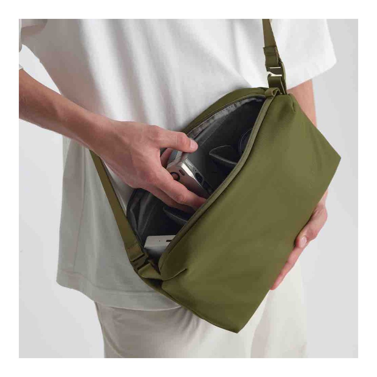 Urth Dolomite Camera Sling (Green) - Anwendungsbeispiel: Person verstaut Gegenstände in offener olivgrüner Umhängetasche.