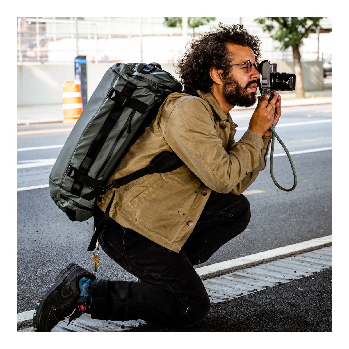 WANDRD HEXAD CARRYALL DUFFEL 40-Liter Wasatch Green - Anwendungsbeispiel: Mann trägt graue Dufflebag als Rucksack und fotografiert kniend.