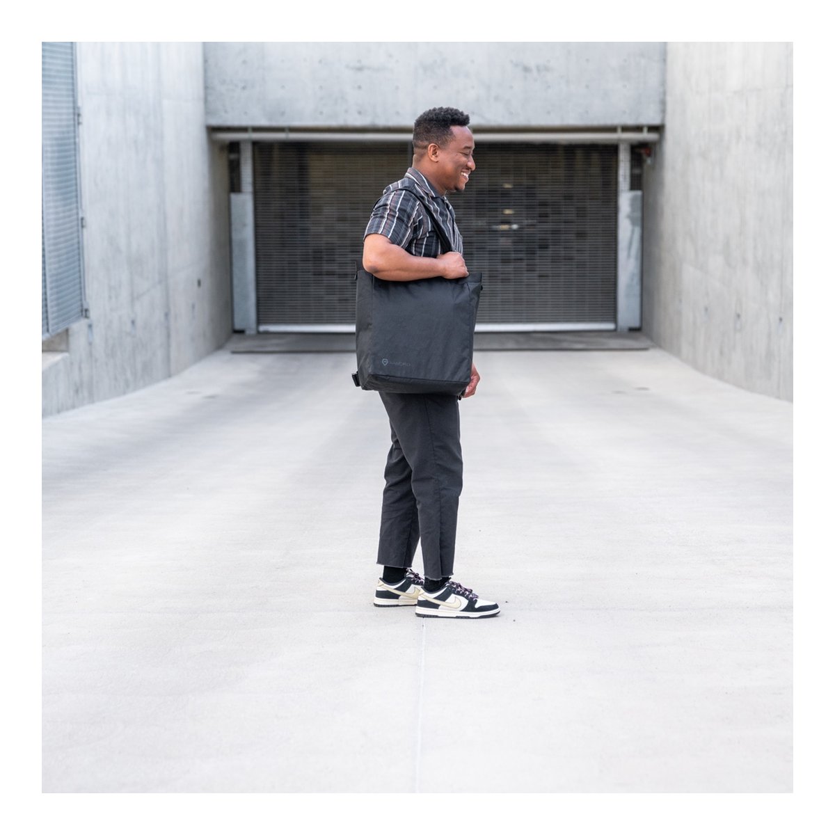 WANDRD Tote Backpack - Anwendungsbeispiel: Mann trägt schwarze Tote Bag seitlich über der Schulter. WANDRD Tote Backpack - Anwendungsbeispiel: Mann trägt schwarze Tote Bag seitlich über der Schulter.