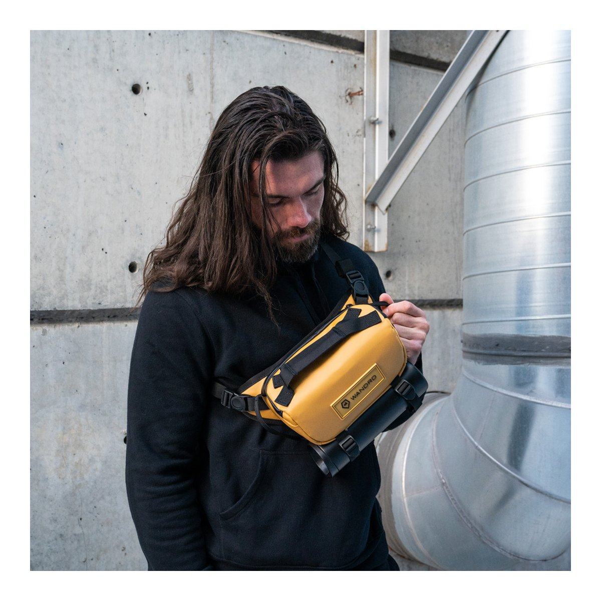 WANDRD ROGUE Sling 3L Dallol Yellow - Anwendungsbeispiel: Mann mit gelber Brusttasche quer über der Brust, justiert sie.