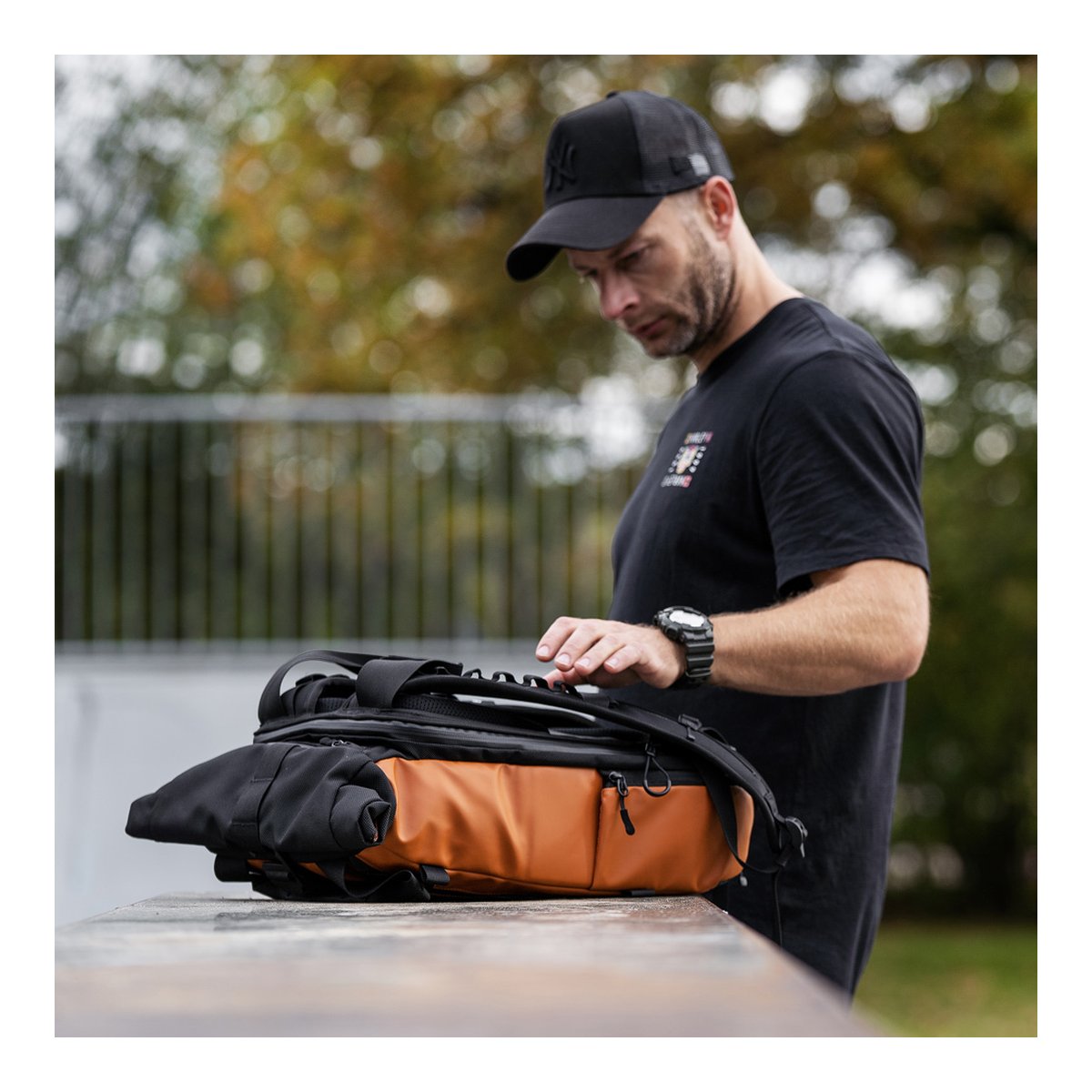 WANDRD PRVKE Lite 11-Liter Sedona Orange - Anwendungsbeispiel: Mann öffnet das Hauptfach des Rucksacks auf einer Bank.