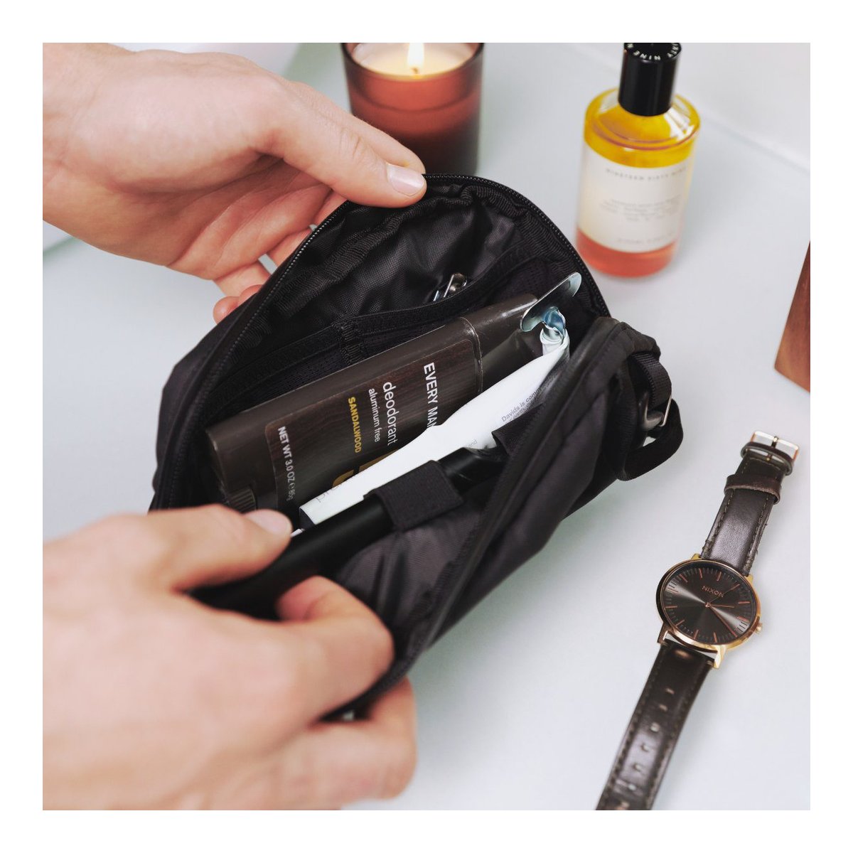 WANDRD Toiletry Bag Medium - Anwendungsbeispiel: Person öffnet Kulturtasche mit Pflegeprodukten wie Deodorant und Zahnpasta.