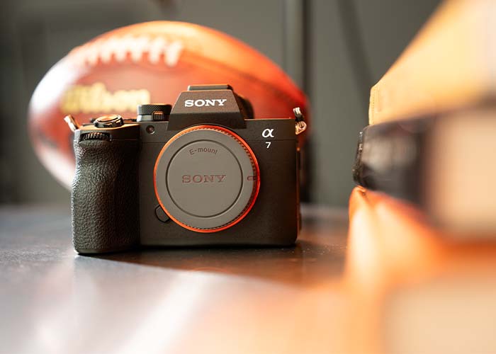 Sony Alpha 7V in Frontansicht als Lifestyle-Aufnahme mit Football im Hintergrund