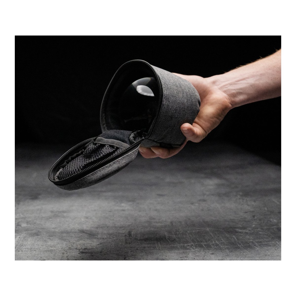 Caruba Tasche für Objektivkugel 60/80mm - Anwendungsbeispiel: Hand hält offene graue Schutzhülle mit Objektiv und Netztasche.