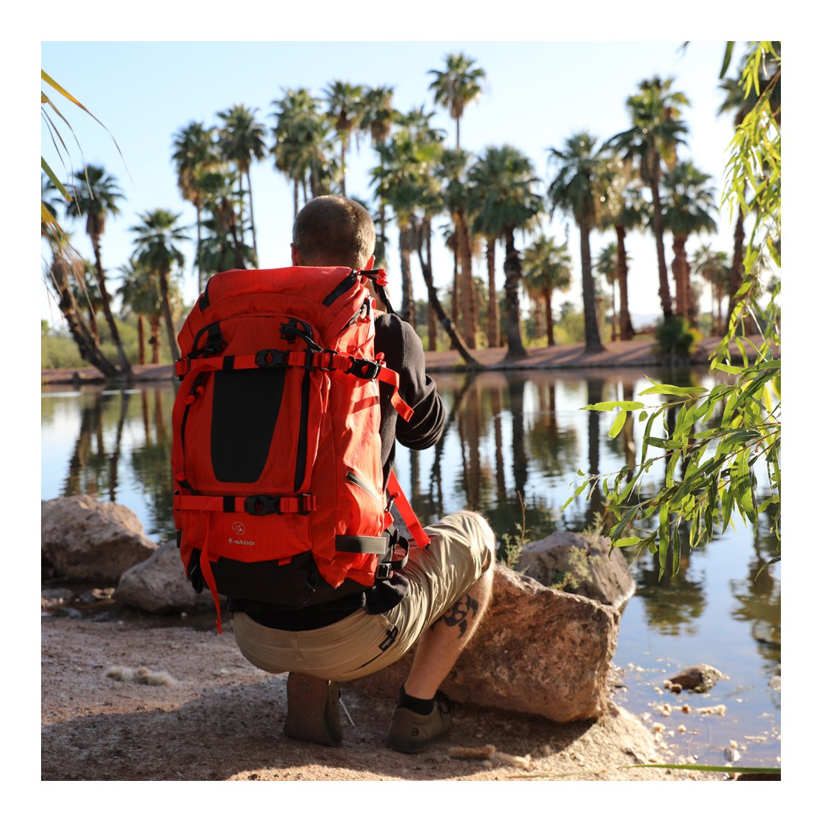 F-Stop DuraDiamond Tilopa - Magma - Rückansicht: Roter Wanderrucksack an Person am Seeufer. F-Stop DuraDiamond Tilopa - Magma - Rückansicht: Roter Wanderrucksack an Person am Seeufer.