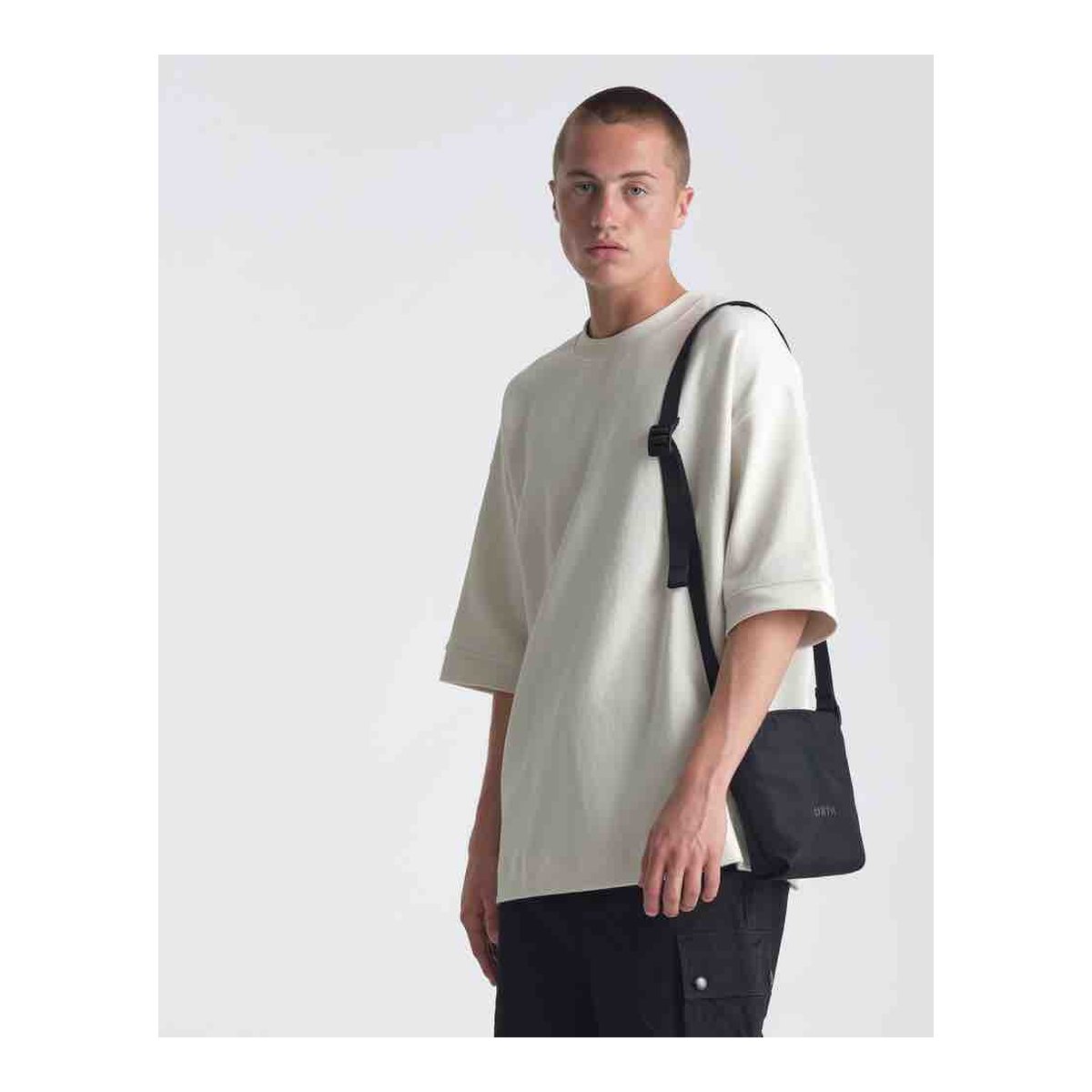 Urth Andesite Camera Pouch (Black) - Anwendungsbeispiel: Mann trägt beiges Oversize T-Shirt und schwarze Umhängetasche. Urth Andesite Camera Pouch (Black) - Anwendungsbeispiel: Mann trägt beiges Oversize T-Shirt und schwarze Umhängetasche.