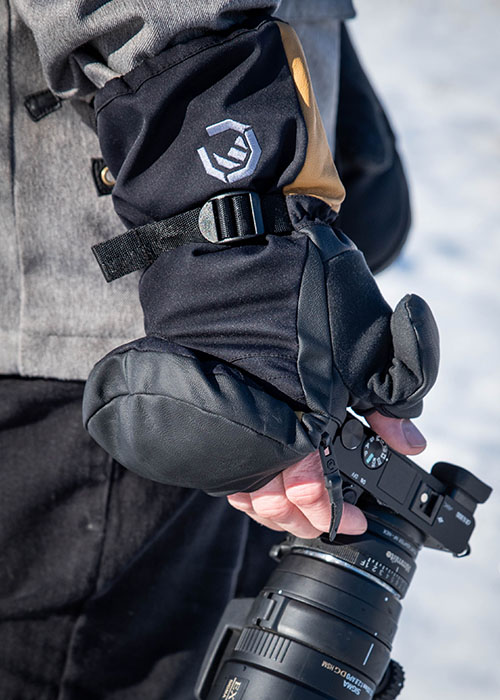 Person hält eine Kamera in der Hand, trägt warme Winterhandschuhe mit aufklappbarer Fingerabdeckung im Schnee.