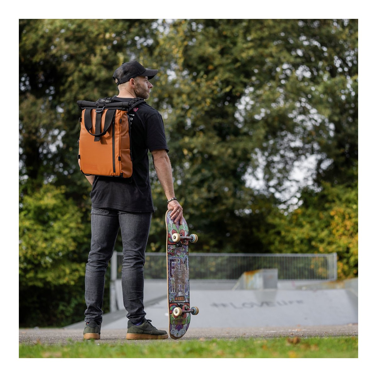 WANDRD PRVKE Lite 11-Liter Sedona Orange - Anwendungsbeispiel: Mann trägt braunen Roll-Top-Rucksack und hält Skateboard.