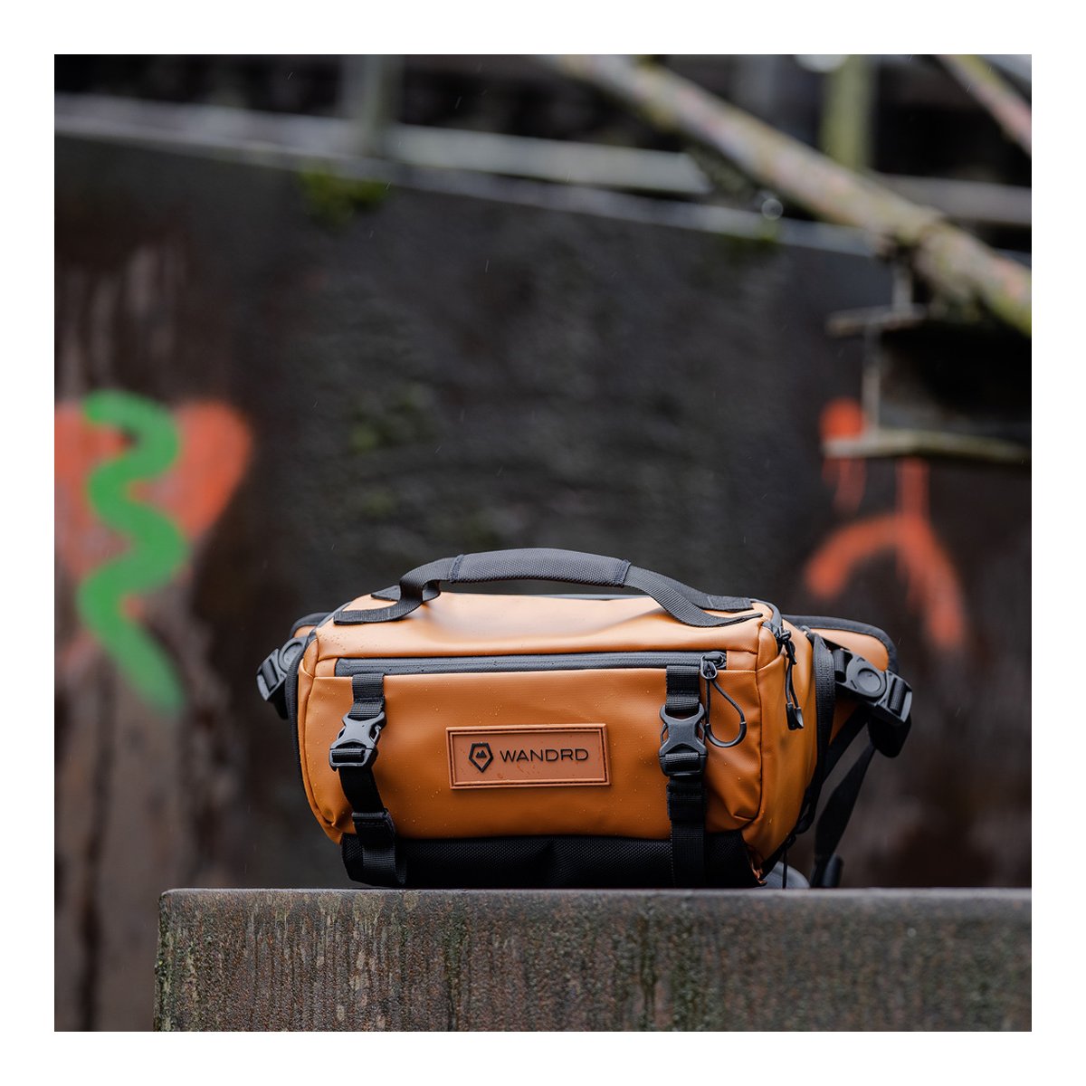 WANDRD ROGUE Sling 6L Sedona Orange - Frontansicht der braunen WANDRD Sling Bag auf nassem Untergrund.