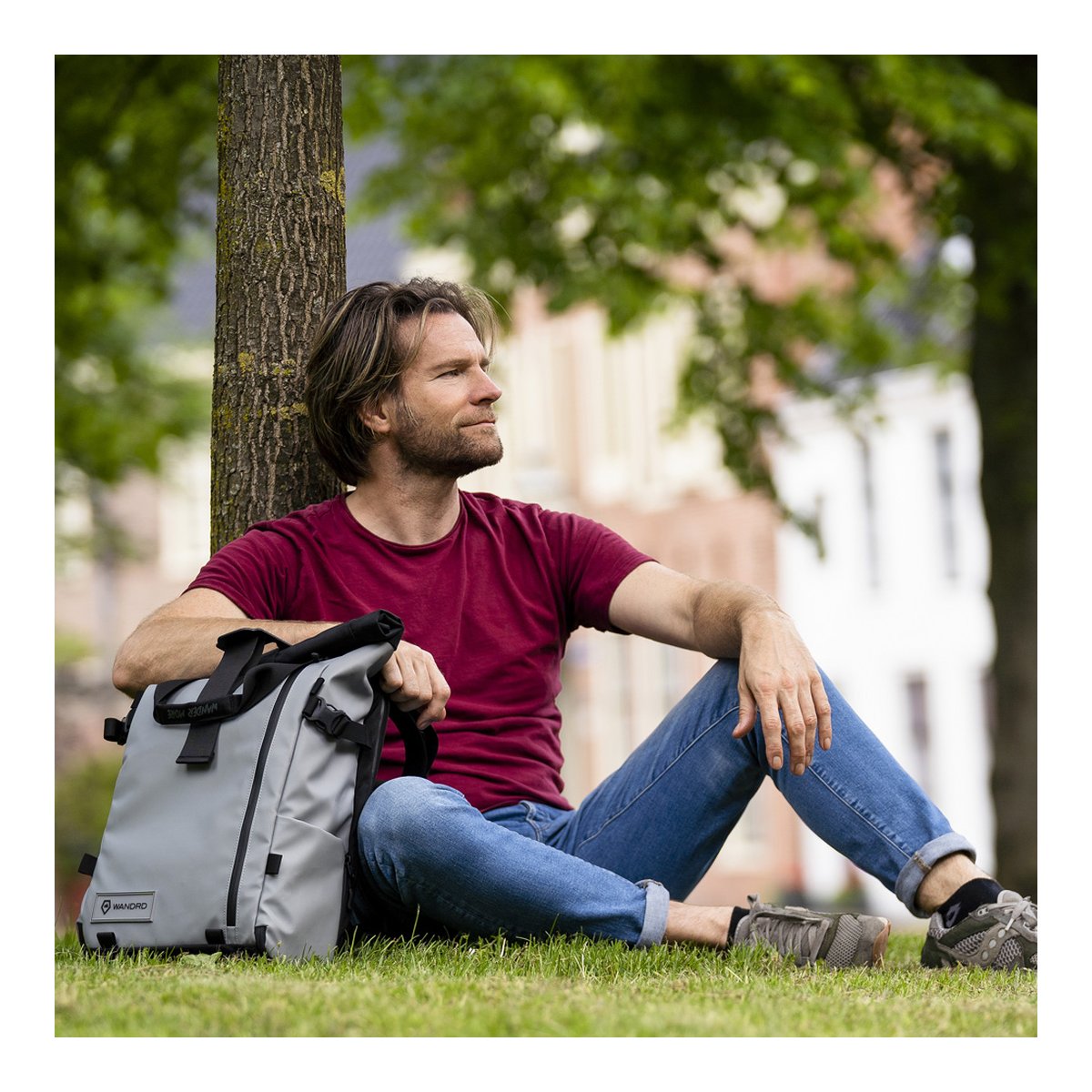 WANDRD PRVKE 31-Liter DisNet Grey Photo Bundle - Anwendungsbeispiel: Mann sitzt mit grauem Rucksack im Gras an Baum gelehnt
