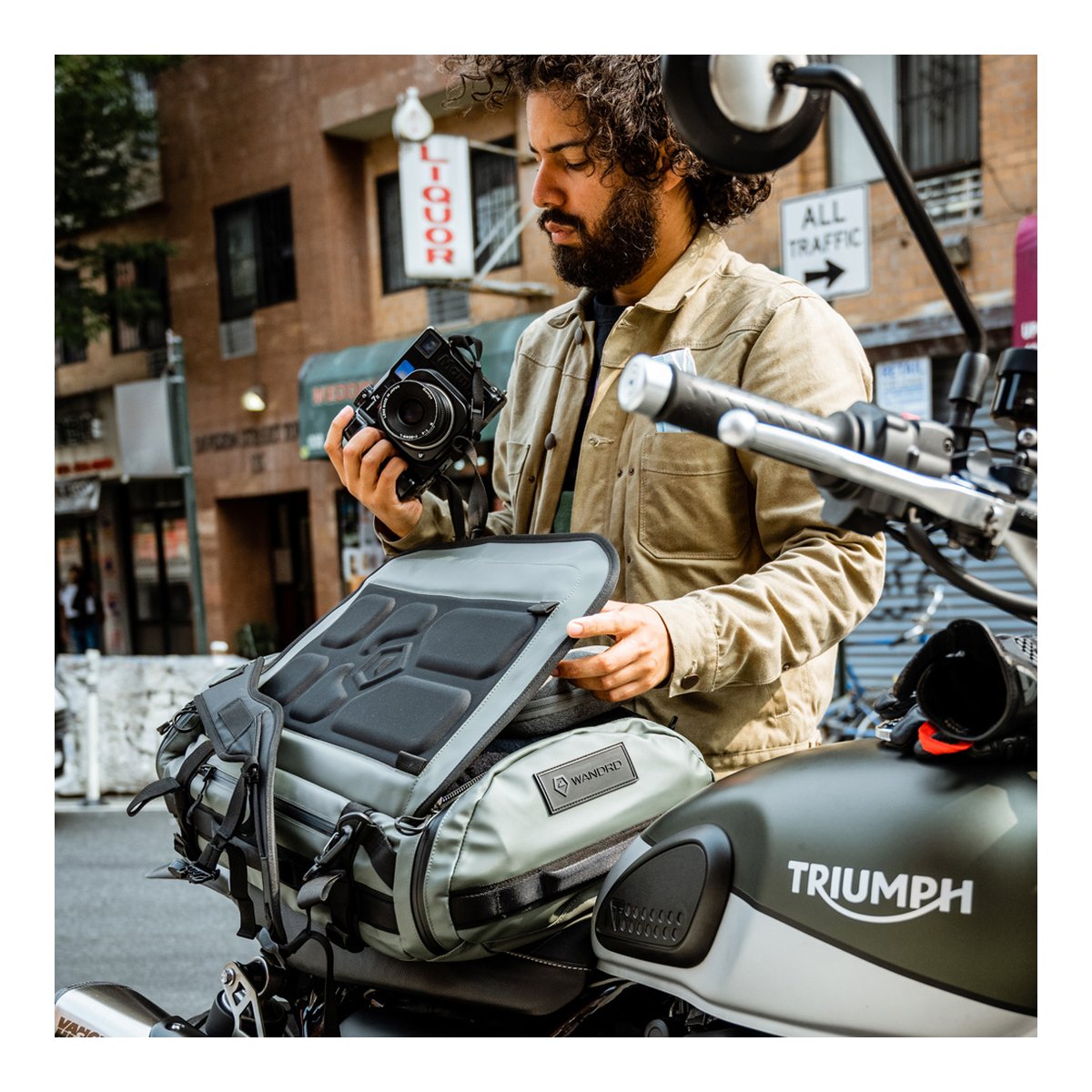 WANDRD HEXAD CARRYALL DUFFEL 40-Liter Wasatch Green - Anwendungsbeispiel: Mann verstaut Kamera in Tanktasche auf Motorrad.