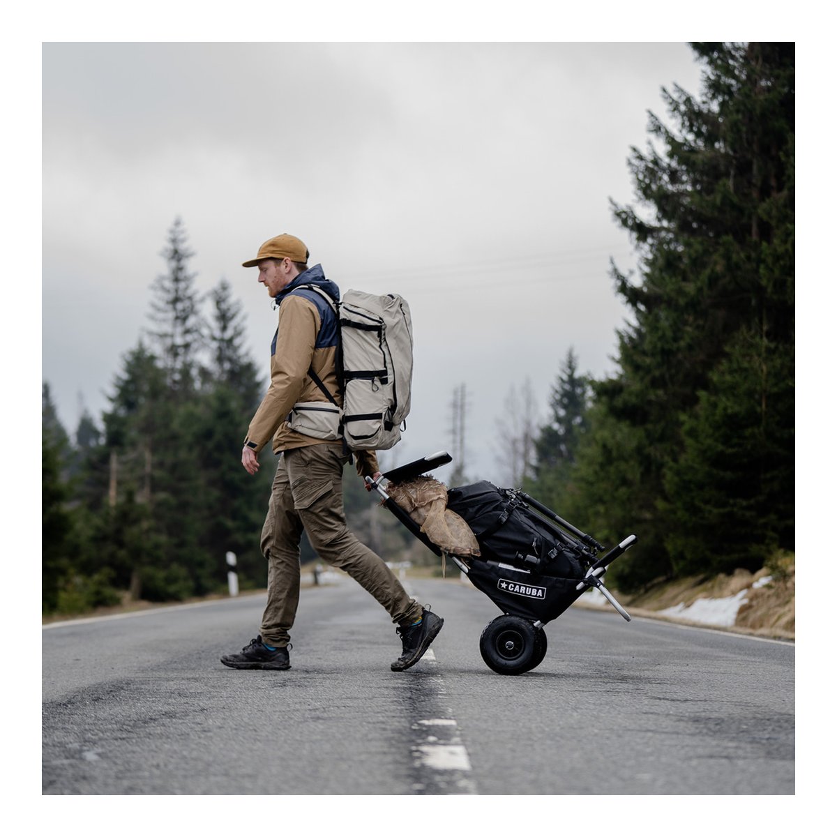 Wandrd Fernweh M/L Tan Photo Bundle - Anwendungsbeispiel: Mann mit Rucksack zieht Outdoor-Transportwagen auf Straße.