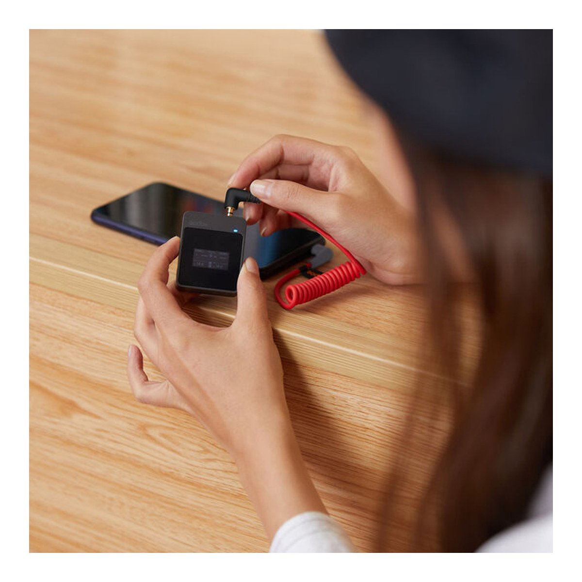 Godox MoveLink M1 - Anwendungsbeispiel: Eine Person verbindet ein kompaktes Audiogerät per Spiralkabel mit einem Smartphone.