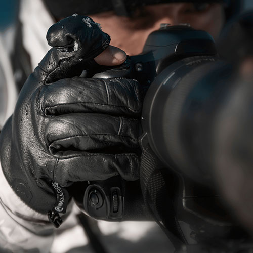 Nahaufnahme einer Hand mit Winter-Fotohandschuh, die den Auslöser einer Kamera bedient.