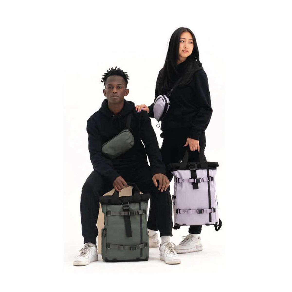 WANDRD PREMIUM ACCESSORY STRAP WASATCH GREEN V2 - Anwendungsbeispiel: Zwei Models präsentieren grüne und lilafarbene Rucksäcke und Umhängetaschen.