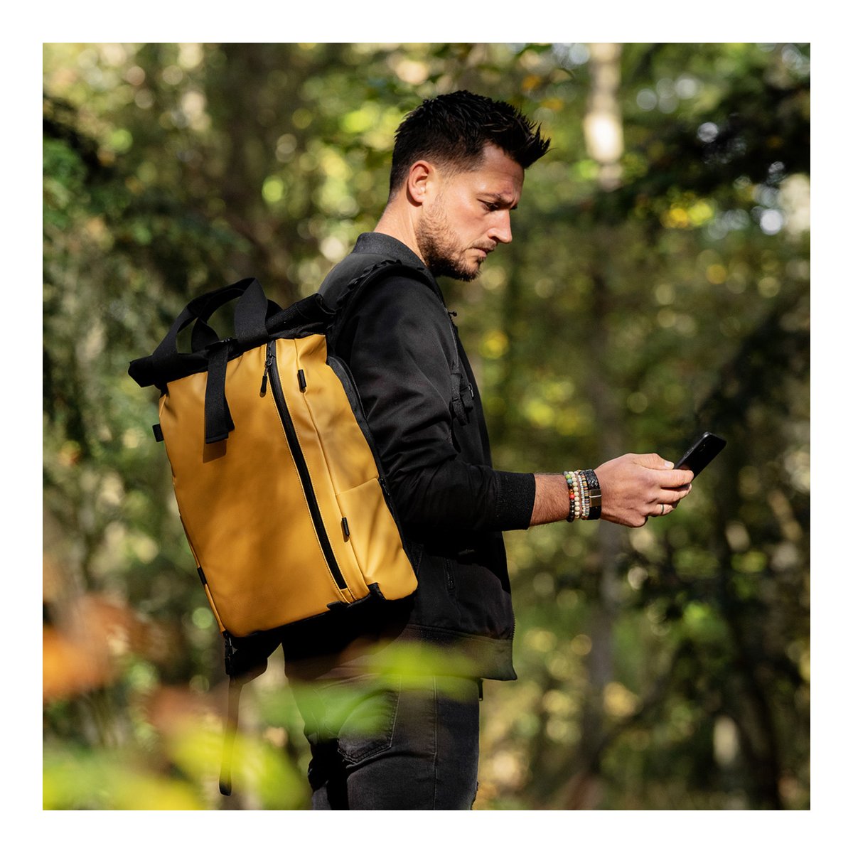 WANDRD PRVKE Lite 11-Liter Dallol Yellow - Anwendungsbeispiel: Mann mit gelbem Rucksack in Seitenansicht, prüft Smartphone im Freien.