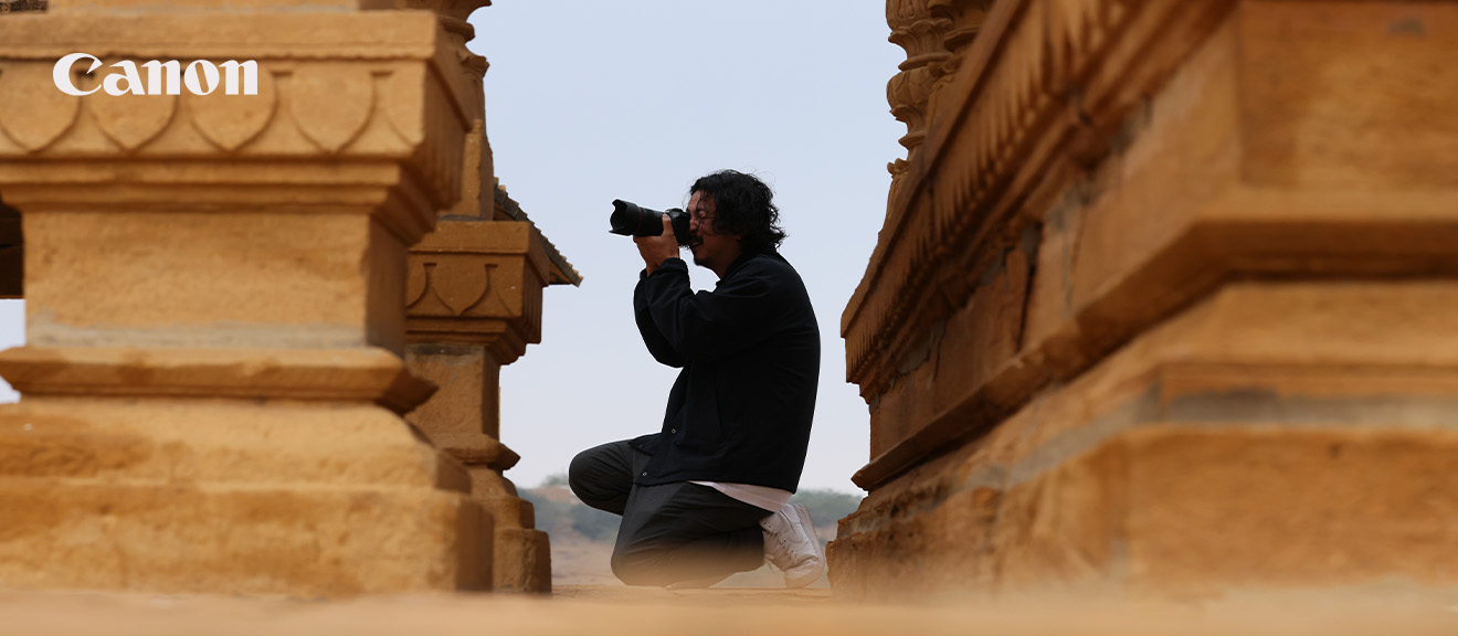 Canon Porträtfotografie mit RF-Objektiven – unterwegs auf Motivsuche Fotograf mit Canon Kamera beim Fotografieren zwischen historischen Steinbauten – ideal für Porträt- oder Reisefotografie