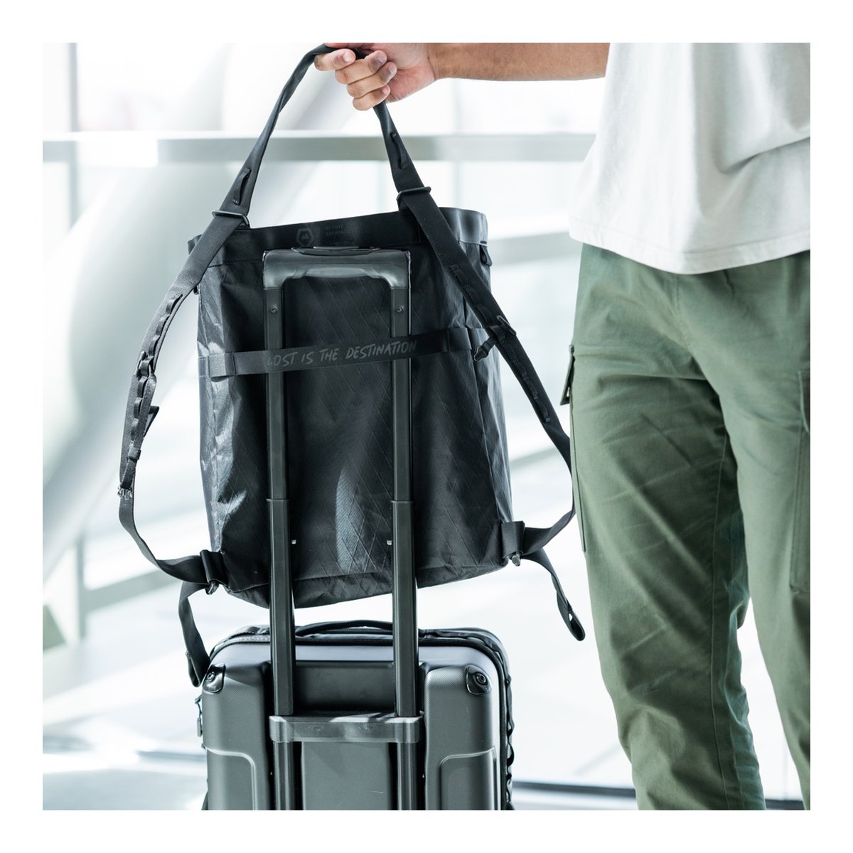 WANDRD Tote Backpack - Anwendungsbeispiel: Tasche auf Rollkoffer-Griff gesteckt und von Hand gehalten. WANDRD Tote Backpack - Anwendungsbeispiel: Tasche auf Rollkoffer-Griff gesteckt und von Hand gehalten.