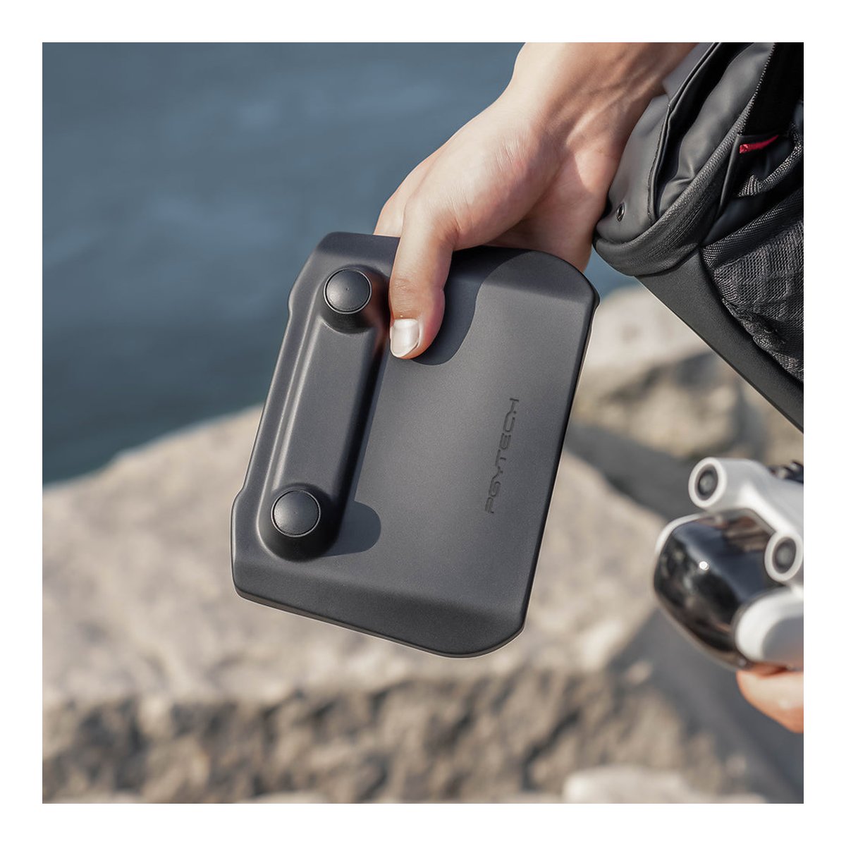 PGYTECH DJI RC Protector - Anwendungsbeispiel: Eine Hand hält eine schwarze PGYTECH-Hülle mit zwei Knöpfen im Outdoor-Setting.
