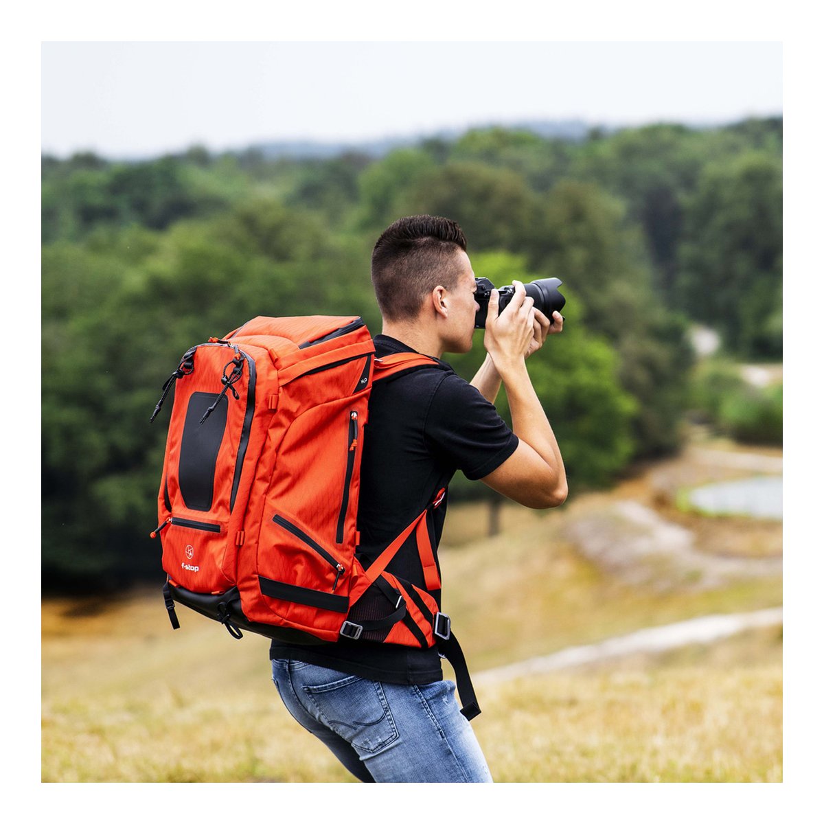 F-Stop DuraDiamond Tilopa - Magma - Anwendungsbeispiel: Rückansicht des orangefarbenen Rucksacks am Mann beim Fotografieren. F-Stop DuraDiamond Tilopa - Magma - Anwendungsbeispiel: Rückansicht des orangefarbenen Rucksacks am Mann beim Fotografieren.