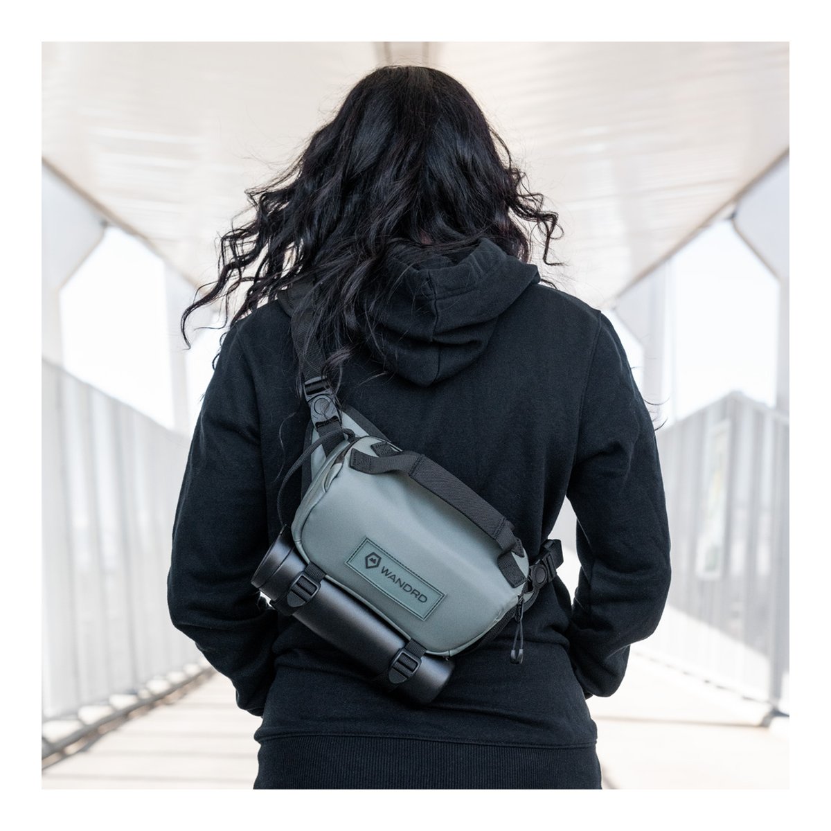WANDRD ROGUE Sling 3L Wasatch Green - Anwendungsbeispiel: Rückansicht der grauen Tasche mit befestigter Trinkflasche, von Person in Hoodie getragen.